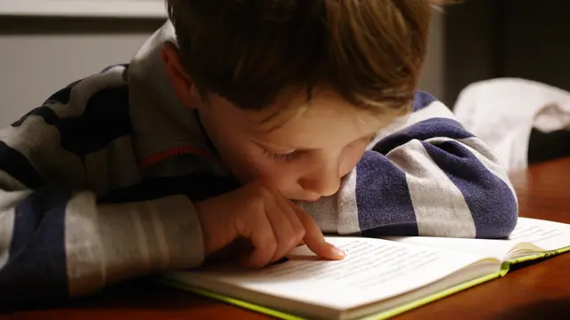 Un bambino che legge seguendo le righe del libro con il dito: uno dei sintomi più comuni della dislessia