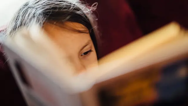 Una bambina assorta nella lettura di un libro, con gli occhi che seguono la pagina: la plusdotazione si nota spesso in una curiosità che non si accontenta