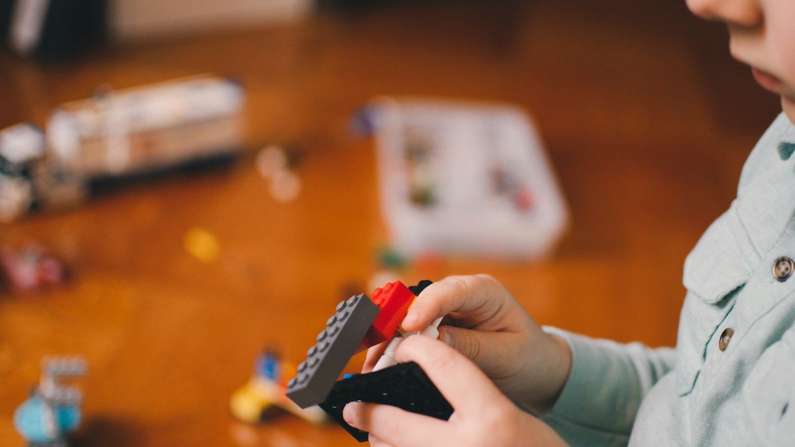 Le mani di un bambino che costruiscono con i mattoncini colorati su un tavolo di legno: nell'alto potenziale cognitivo l'impegno su ciò che appassiona è totale